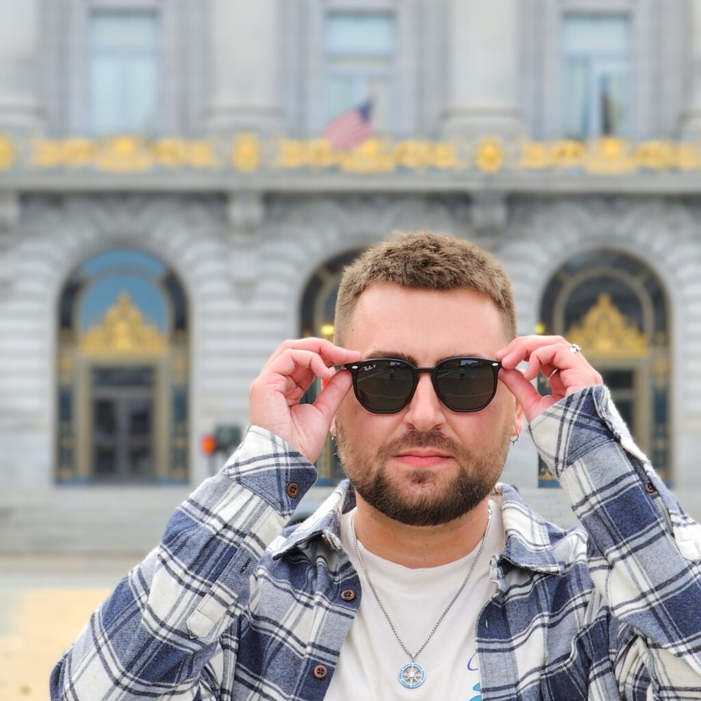 Ty taking off sunglasses in front of SF city hall with a delightful about of bokeh.